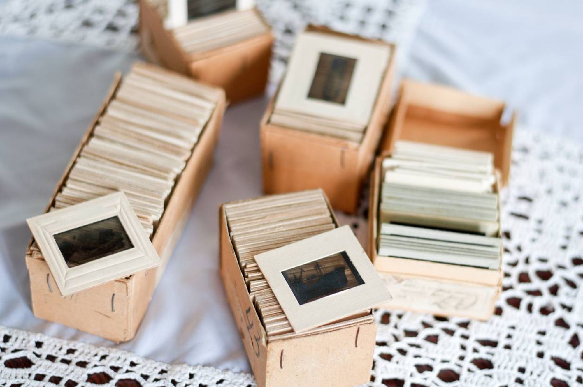 Boxes of vintage photo slides on a lace tablecloth.